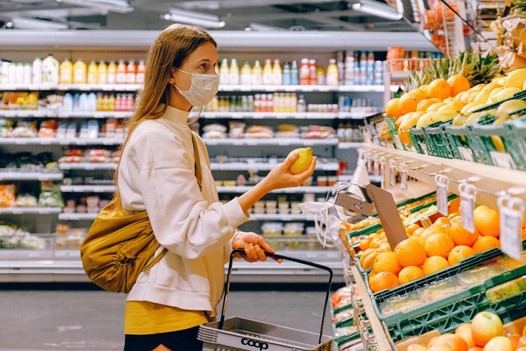 woman holding orange and looking at fruit isle in grocery store